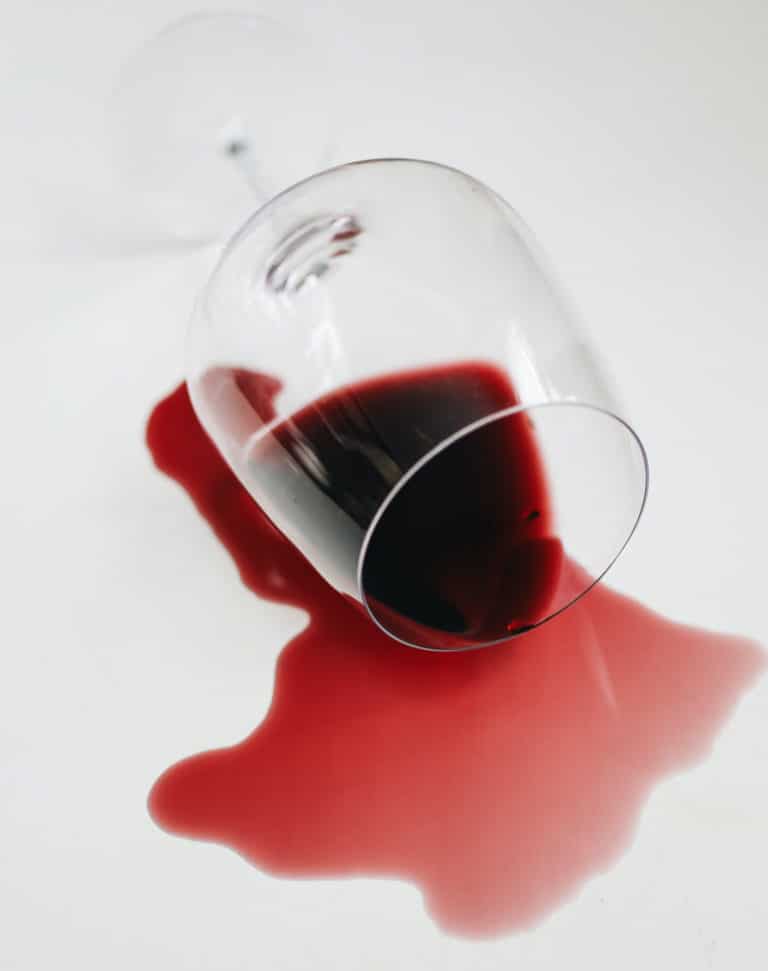 A glass of red wine on it's side with the contents spilling out